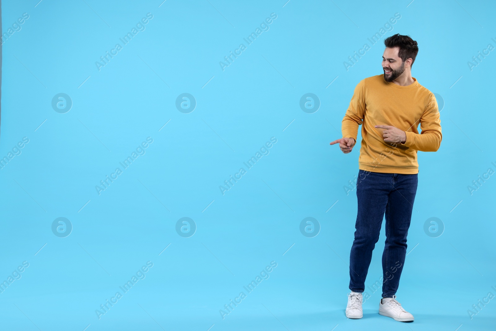 Photo of Happy young man pointing at something on light blue background, space for text