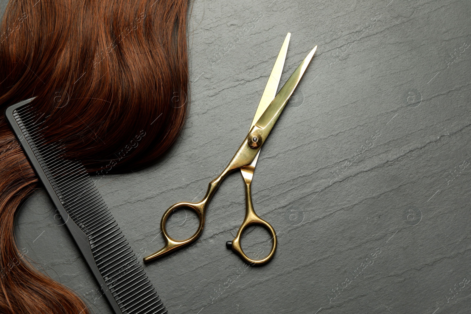 Photo of Professional hairdresser scissors and comb with brown hair strand on dark grey table, top view. Space for text
