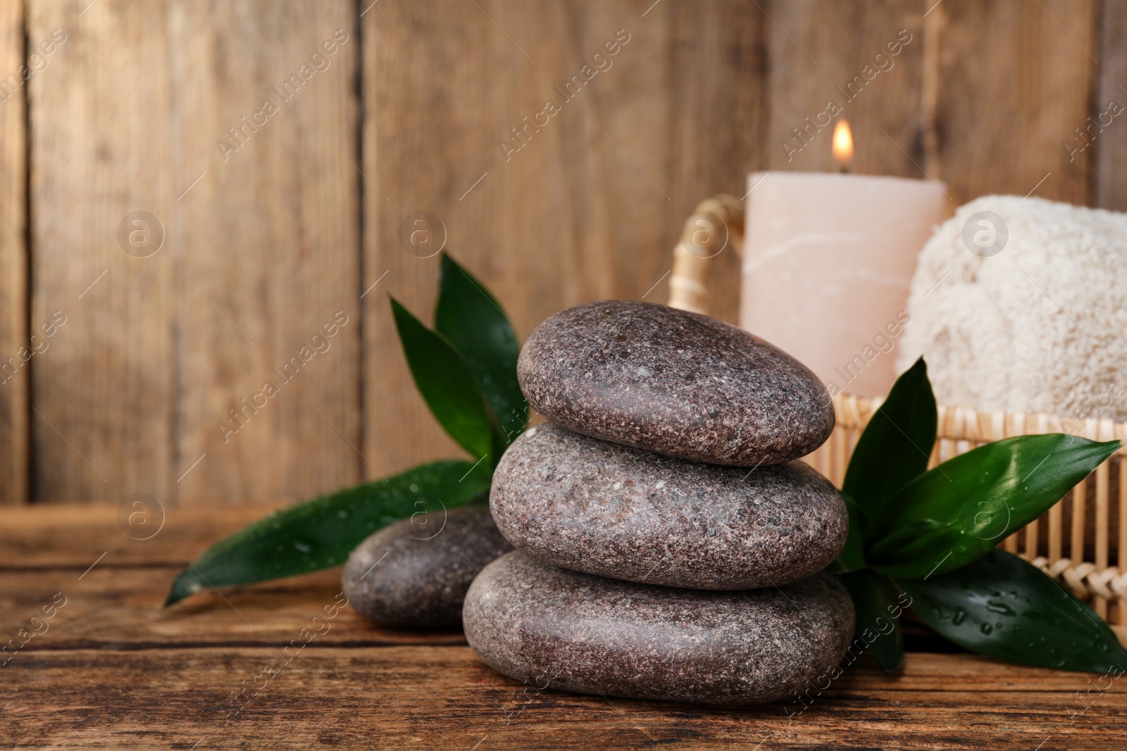 Photo of Stacked spa stones, bamboo leaves, candle and towel on wooden table. Space for text