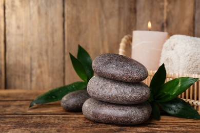 Stacked spa stones, bamboo leaves, candle and towel on wooden table. Space for text