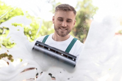 Photo of Male cleaner wiping window glass with squeegee from outside