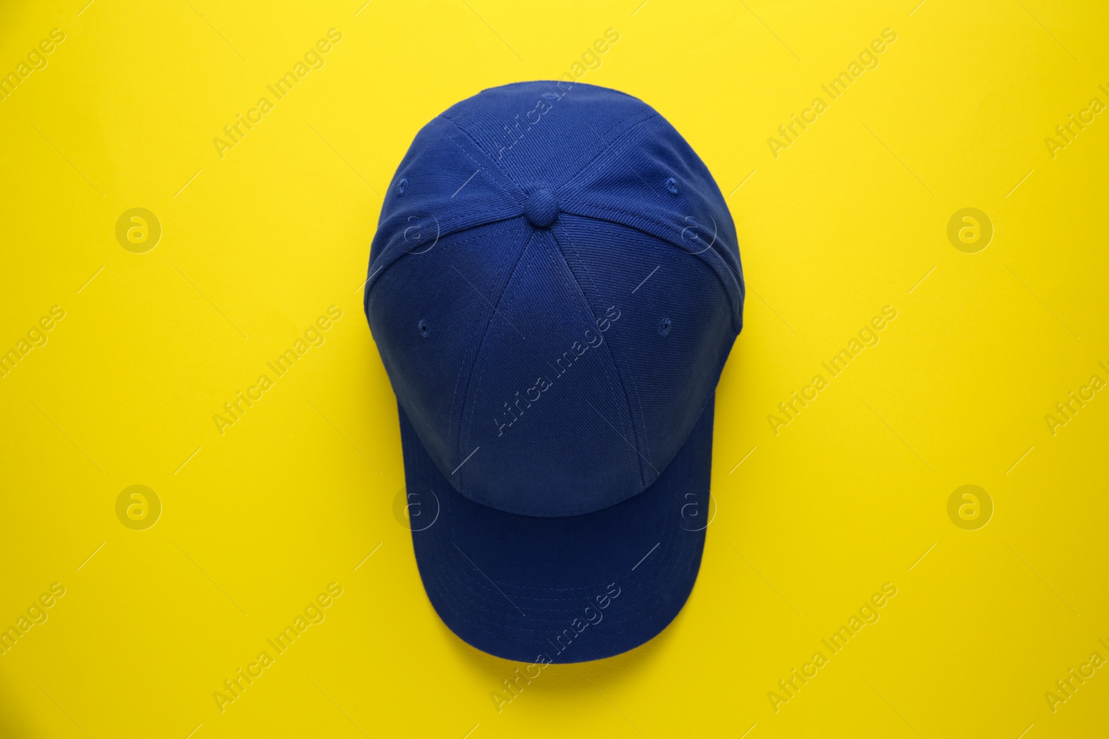 Photo of Stylish blue baseball cap on yellow background, top view