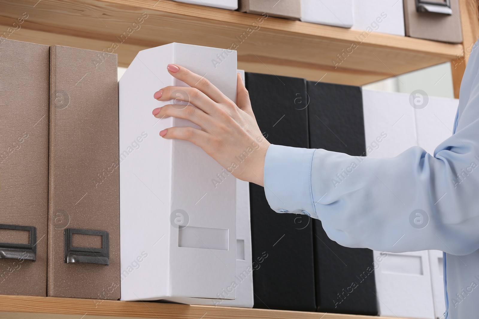 Photo of Woman taking folder with documents from shelf in office, closeup