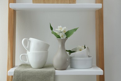 Photo of Beautiful jasmine flowers and tableware on shelving unit in kitchen