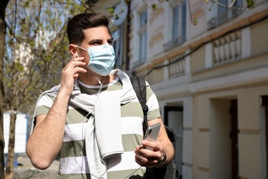 Photo of Man in protective mask listening to audiobook on city street