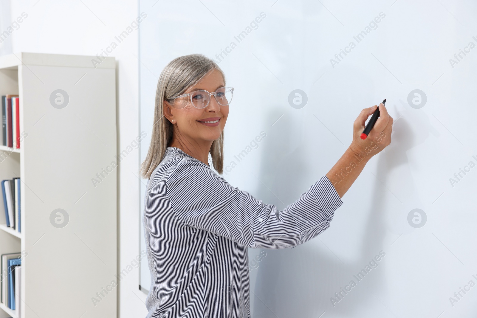 Photo of Professor explaining something with marker at whiteboard in classroom