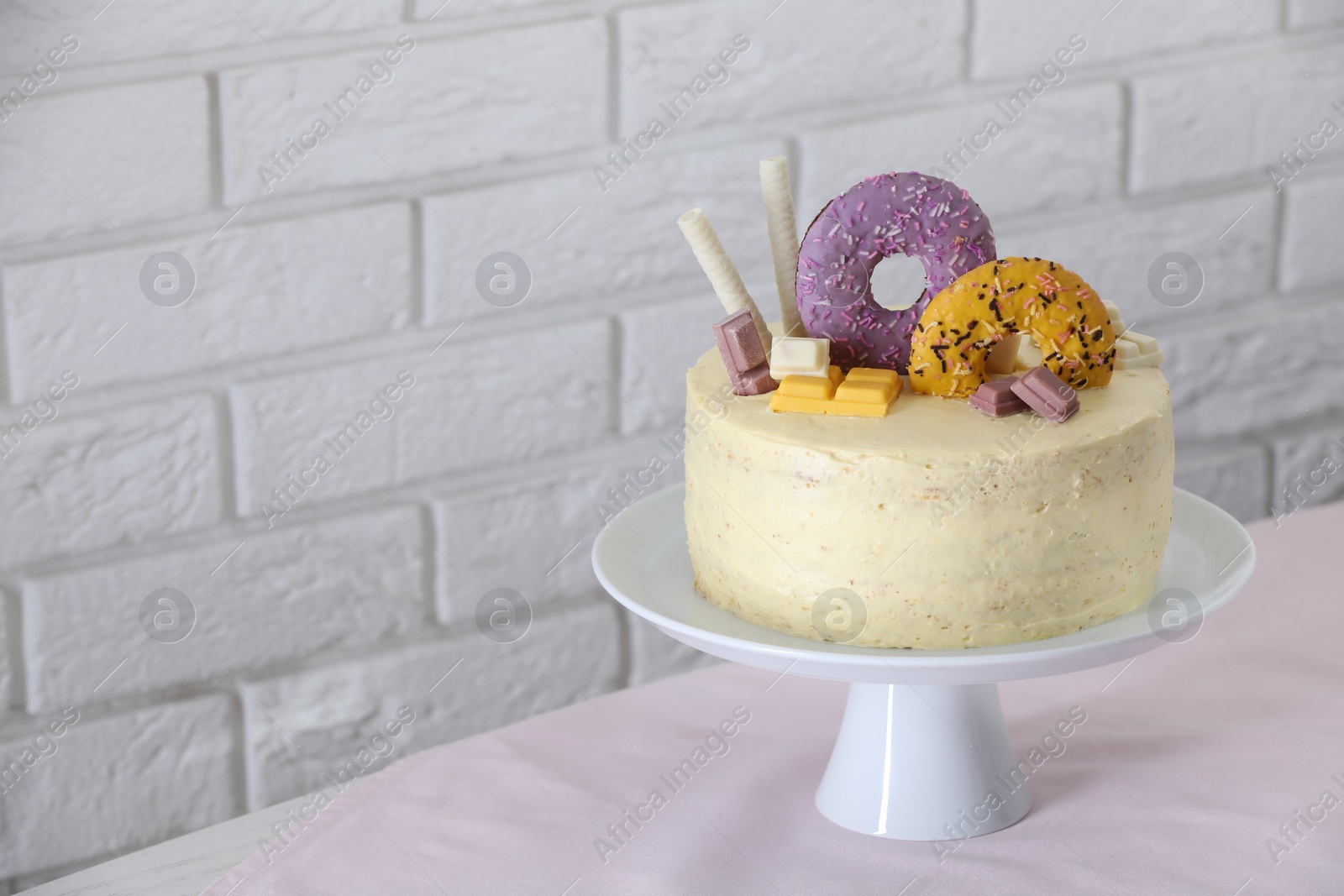 Photo of Delicious cake decorated with sweets on table near white brick wall, space for text