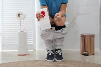 Photo of Boy holding toilet paper with blood stain in rest room, closeup. Hemorrhoid concept