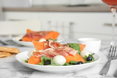 Photo of Fresh melon with prosciutto, mozzarella and arugula on marble table