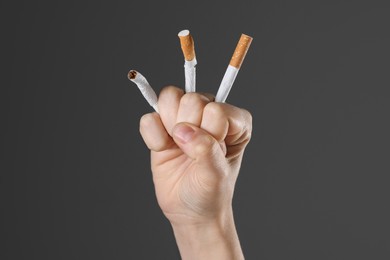 Stop smoking concept. Woman crushing cigarettes on gray background, closeup