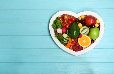 Photo of Heart shaped plate with fresh fruits and vegetables on wooden background, top view. Cardiac diet
