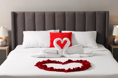 Photo of Honeymoon. Swans made with towels and heart of beautiful rose petals on bed in room