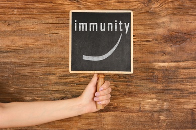 Image of Man holding small chalkboard with word Immunity on wooden background, closeup