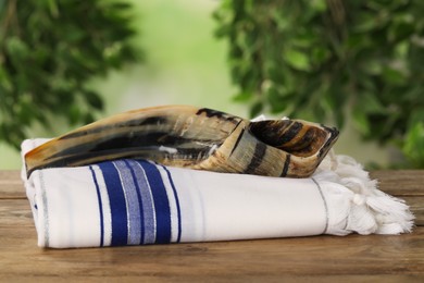 Photo of Shofar and Tallit on wooden table outdoors. Rosh Hashanah holiday attributes