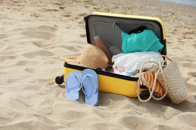 Photo of Open suitcase with beach items on sandy coast