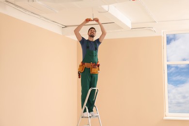 Electrician in uniform with pliers repairing ceiling wiring indoors