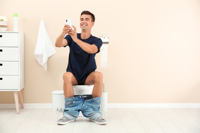 Photo of Young man taking selfie while sitting on toilet bowl at home