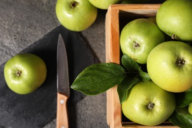 Photo of Ripe green apples with water drops, cutting board and knife on grey table, flat lay