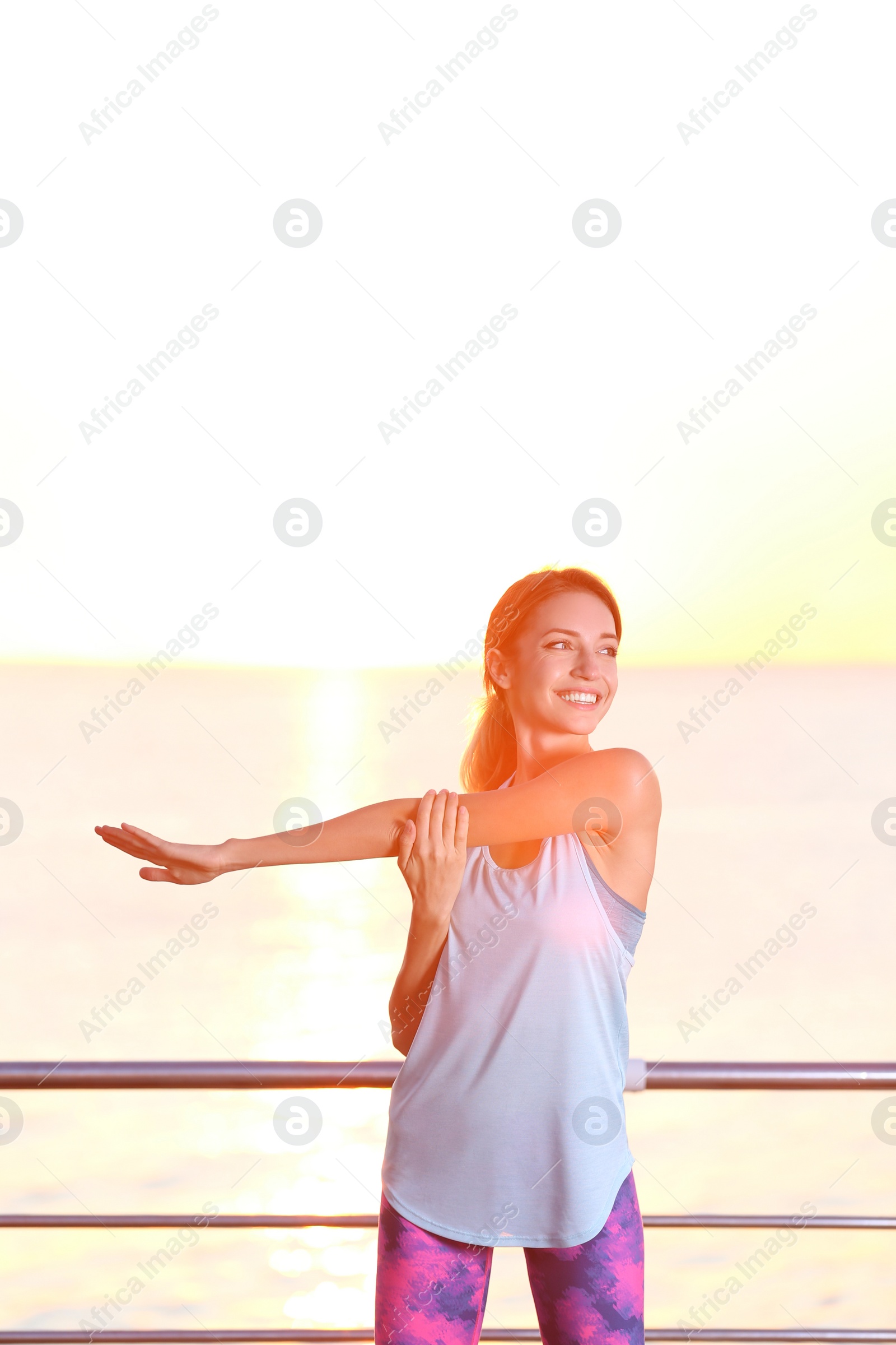 Photo of Young woman doing fitness exercises on pier in morning