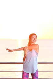 Young woman doing fitness exercises on pier in morning