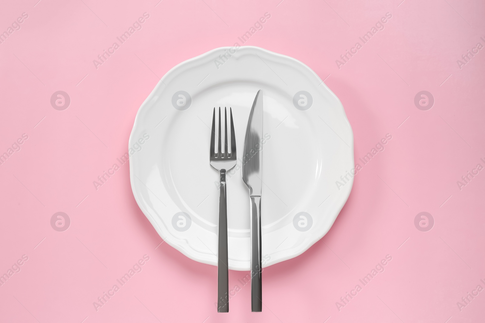 Photo of Clean plate with cutlery on pink background, top view