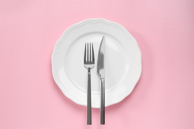 Clean plate with cutlery on pink background, top view