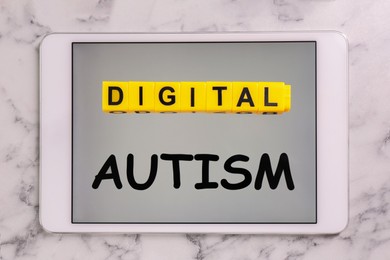 Photo of Addictive behavior. Phrase Digital Autism made of yellow cubes and tablet on white marble table, top view