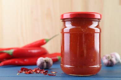 Photo of Spicy chili sauce in jar, garlic and peppers on blue wooden table, space for text