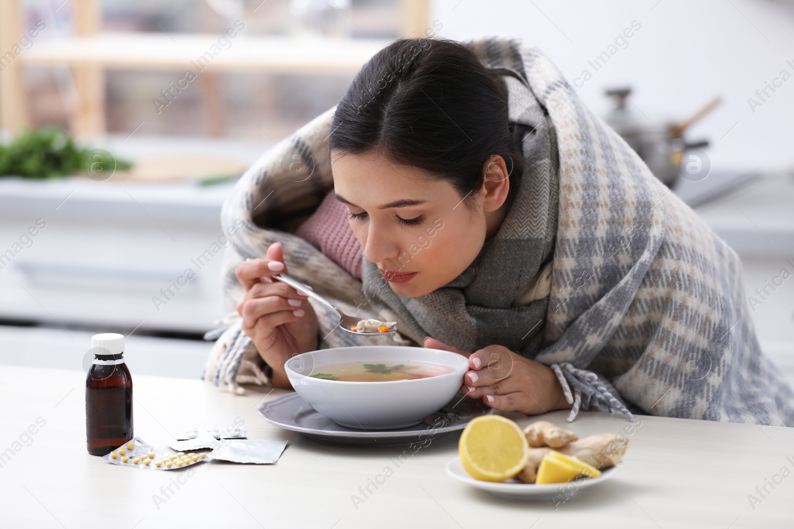 Photo of Sick young woman eating soup to cure flu at table in kitchen