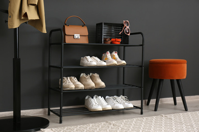 Shelving rack with stylish shoes and accessories near black wall at home. Idea for hallway interior design