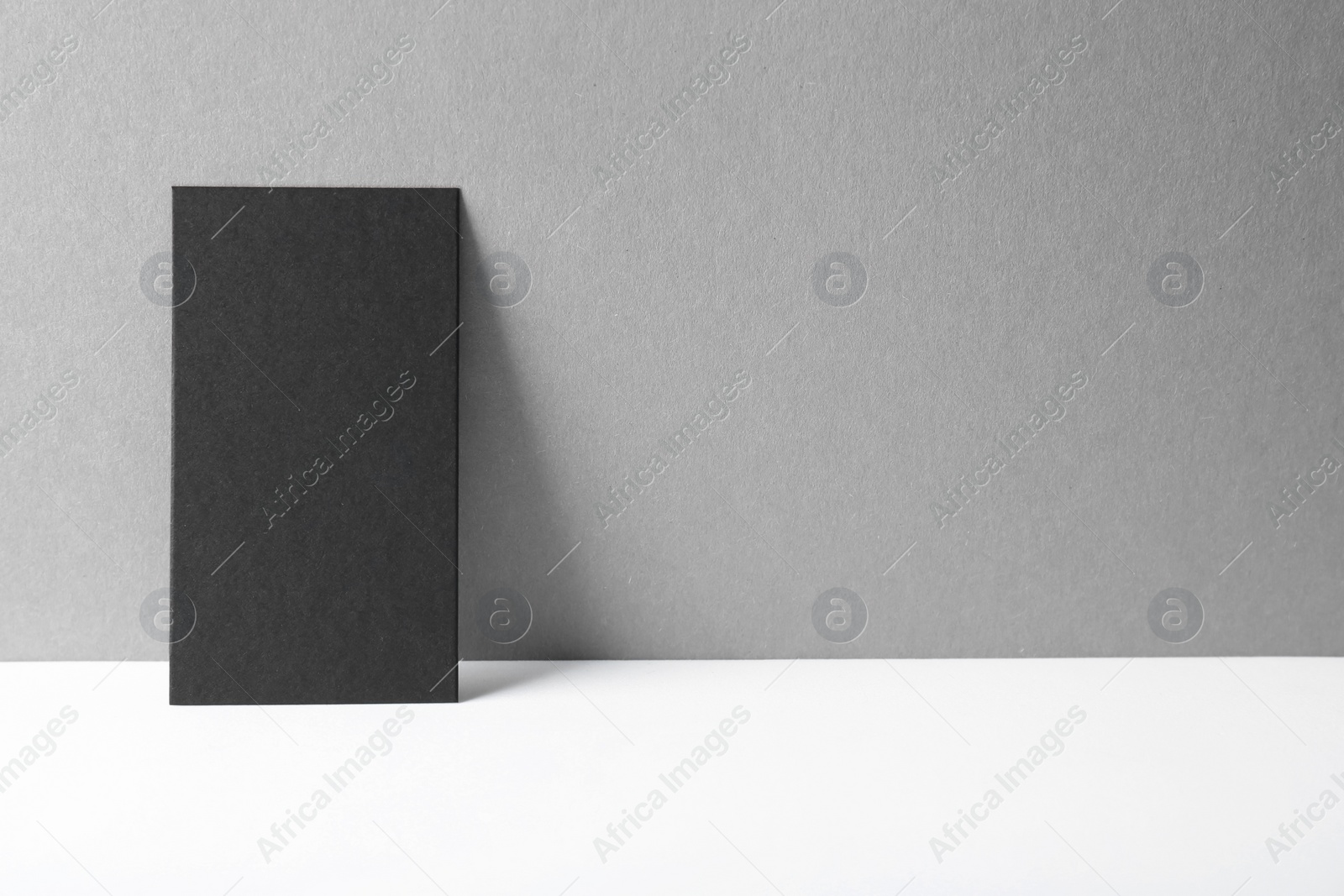 Photo of Blank black business card on white table against grey background. Mockup for design