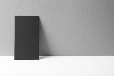 Photo of Blank black business card on white table against grey background. Mockup for design