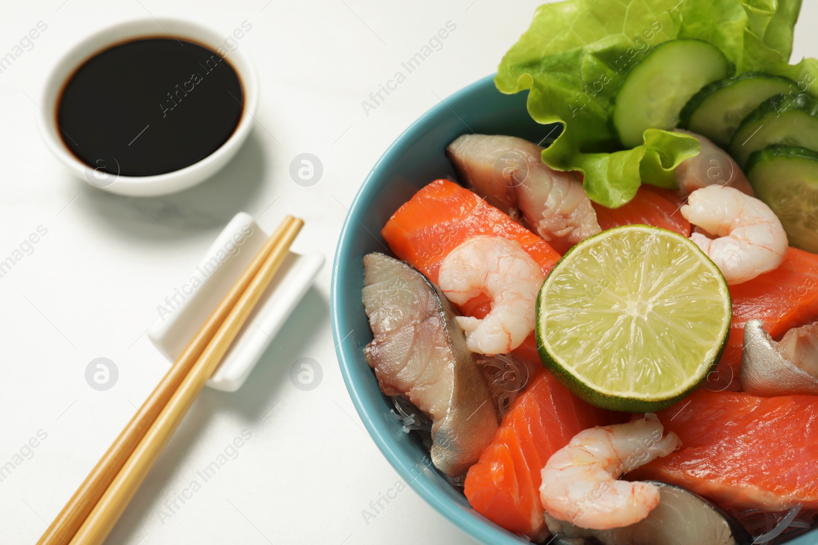 Photo of Delicious mackerel, shrimps and salmon served with lettuce, lime, cucumbers and soy sauce on white marble table, closeup. Tasty sashimi dish