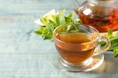 Photo of Cup with hot aromatic mint tea and fresh leaves on table