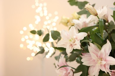 Photo of Bouquet of beautiful lily flowers against beige background with blurred lights, closeup. Space for text