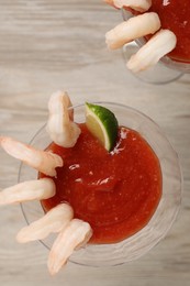 Photo of Tasty shrimp cocktail with sauce and lime in glasses on wooden table, flat lay