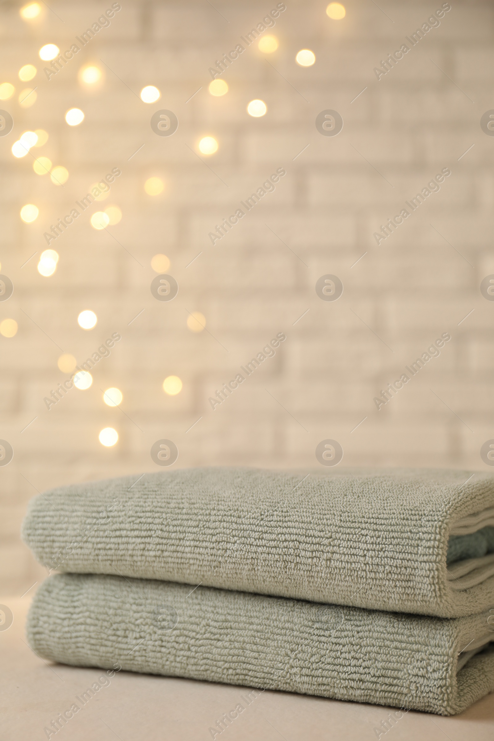Photo of Stacked soft towels on white table near brick wall indoors, closeup. Space for text