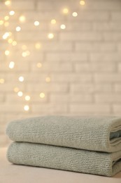 Stacked soft towels on white table near brick wall indoors, closeup. Space for text