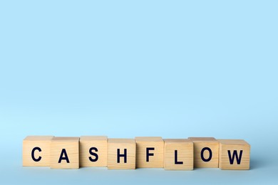 Image of Wooden cubes with phrase Cash FLow on light blue background. Space for text