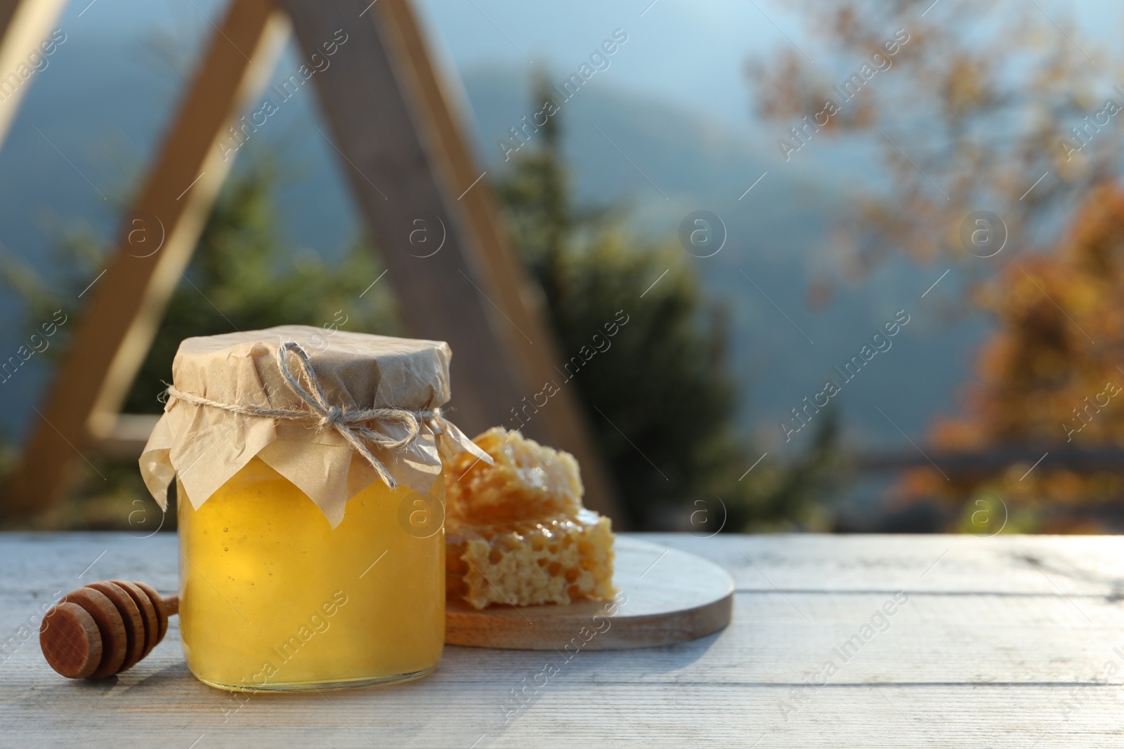 Photo of Fresh aromatic honey and combs on grey wooden table outdoors. Space for text