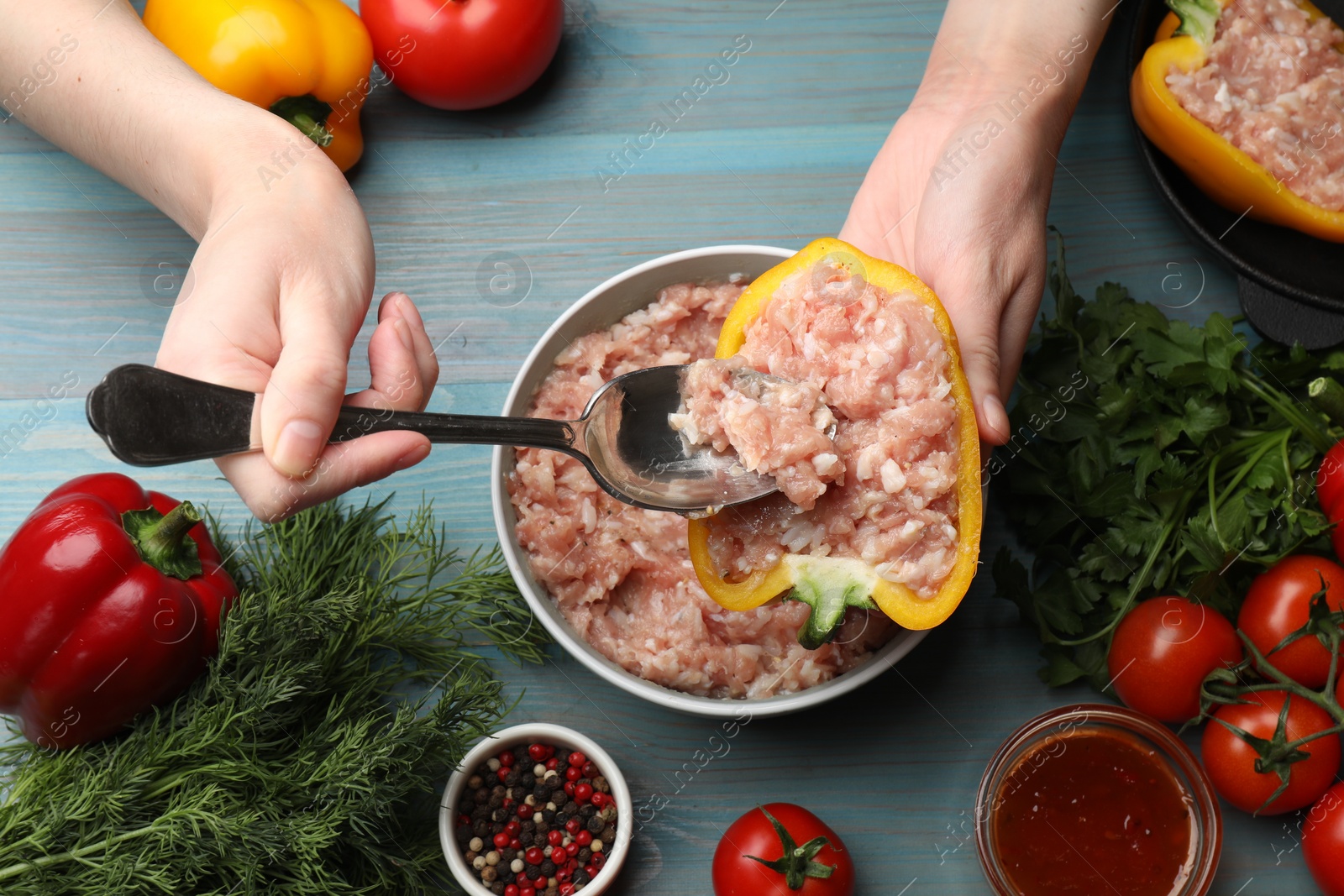 Photo of Woman making stuffed peppers with ground meat at light blue wooden table, top view