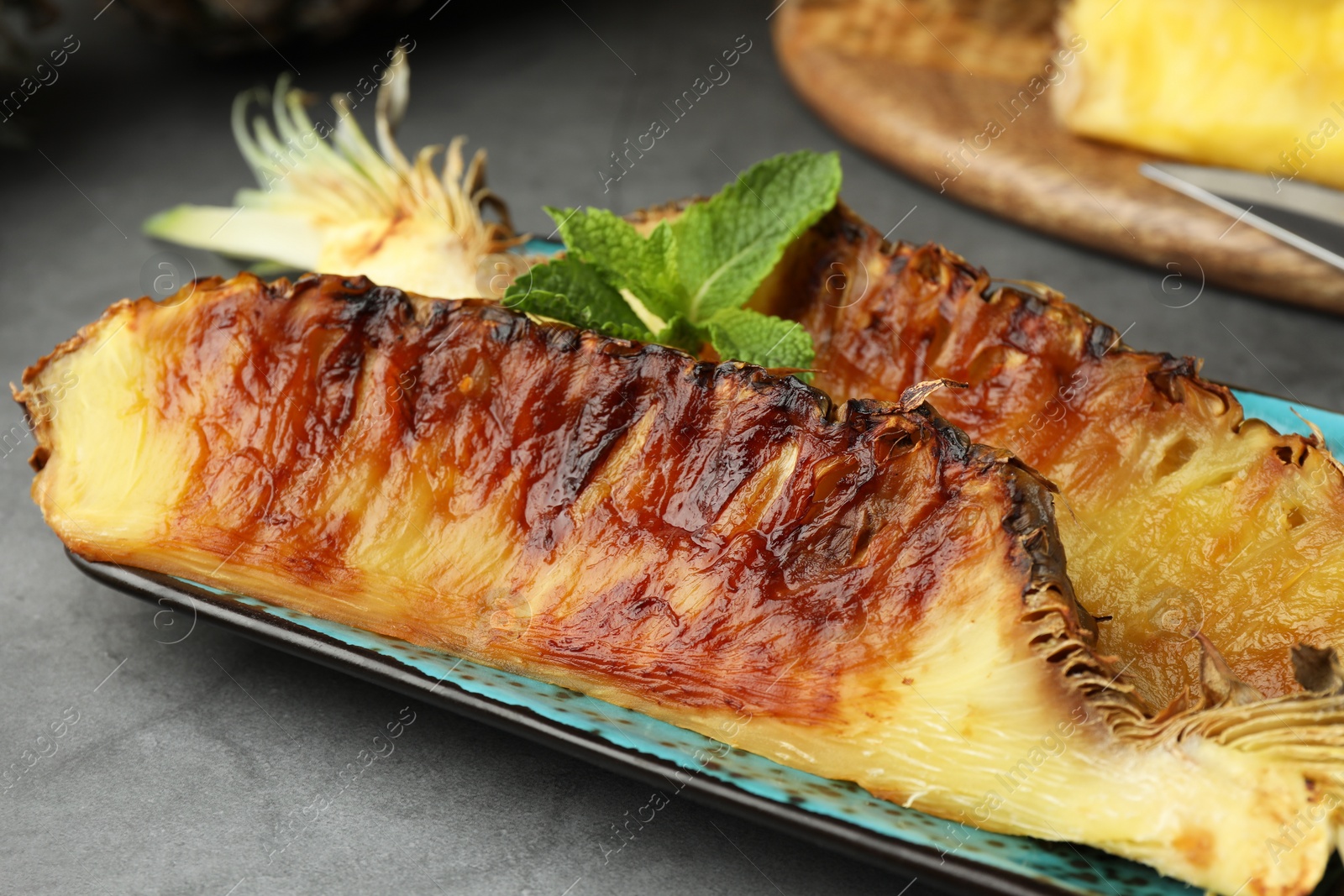 Photo of Plate with tasty grilled pineapple pieces and mint leaves on grey textured table, closeup