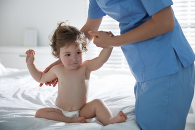 Orthopedist examining little baby on bed indoors