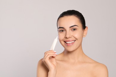 Photo of Beautiful young woman applying gel on skin under eye against light grey background, space for text