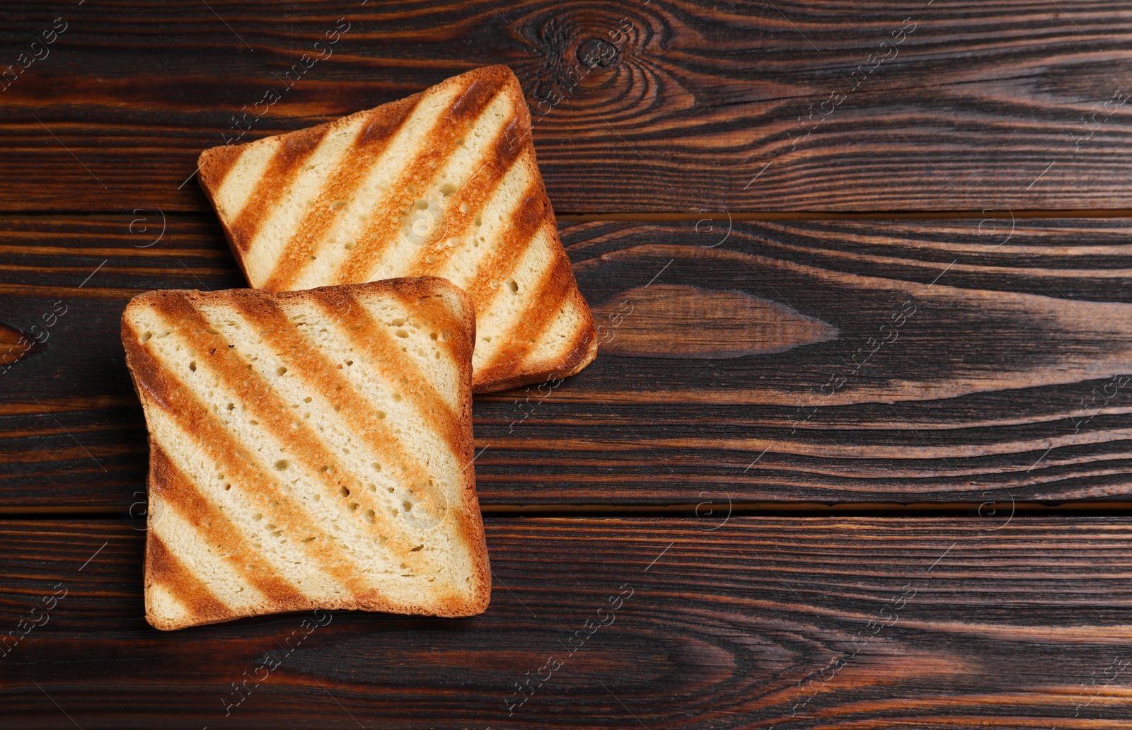 Photo of Slices of tasty toasted bread on wooden table, flat lay. Space for text