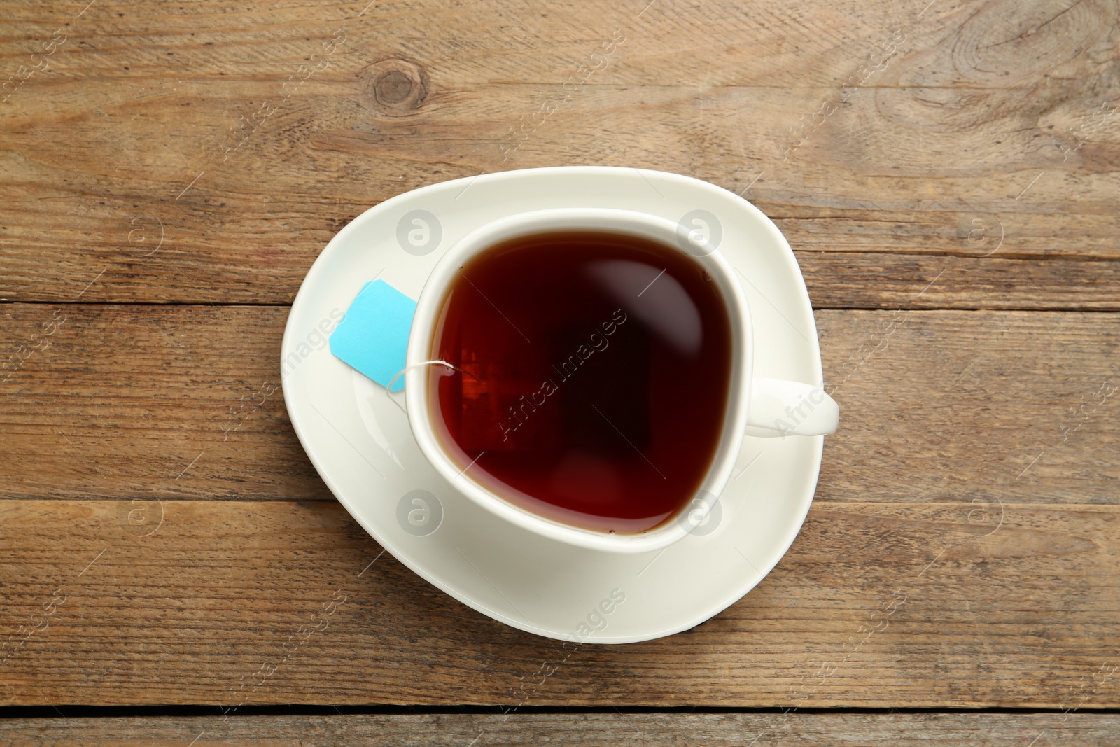 Photo of Tea bag in ceramic cup of hot water on wooden table, top view