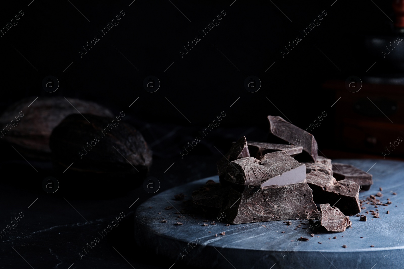 Photo of Pieces of tasty dark chocolate on grey marble board, closeup
