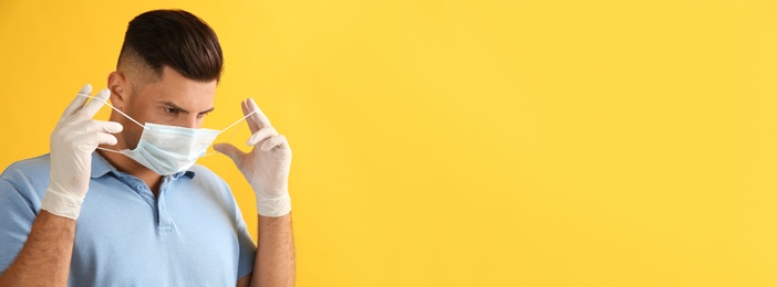 Photo of Man in medical gloves putting on protective face mask against yellow background. Space for text