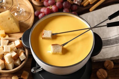 Pot of tasty cheese fondue, forks with bread pieces and snacks on table, above view