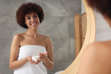 Photo of Beautiful young woman holding body cream indoors